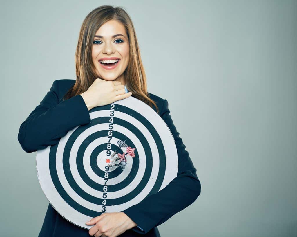 Business woman smiling and holding big target of darts.