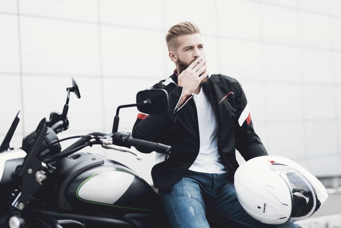 A young guy with a beard sits on his electric motorcycle.