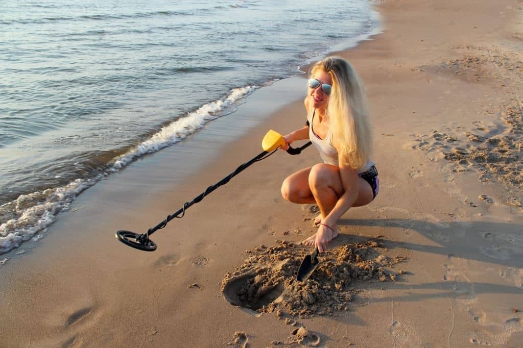 blonde girl in sunglasses with metal detector on the beach