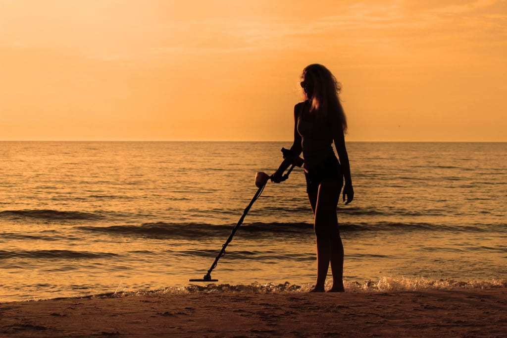 silhuete girl with metal detector on the beach on the sunset