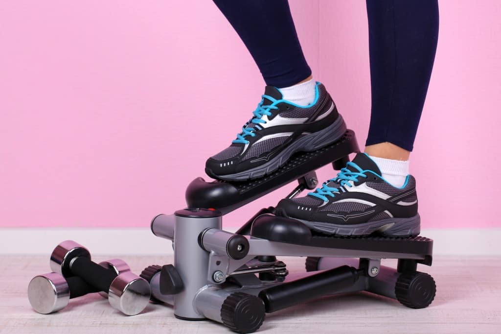 Woman doing exercise on stepper. Close-up on legs.
