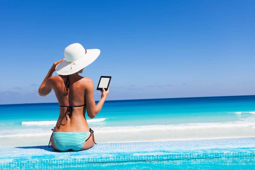 Girl with white hat reads kindle on beach